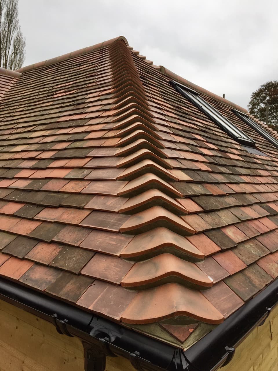 Close-up of a hipped roof with multi-tonal red clay plain tiles, bonnet hip tiles and a skylight