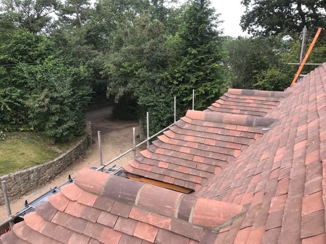 Newly laid red clay tiled roof with curved bonnet hip tiles and scaffolding