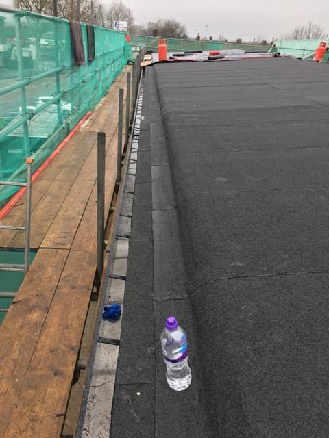 Flat roof under construction with dark bitumen membrane, scaffolding and safety netting