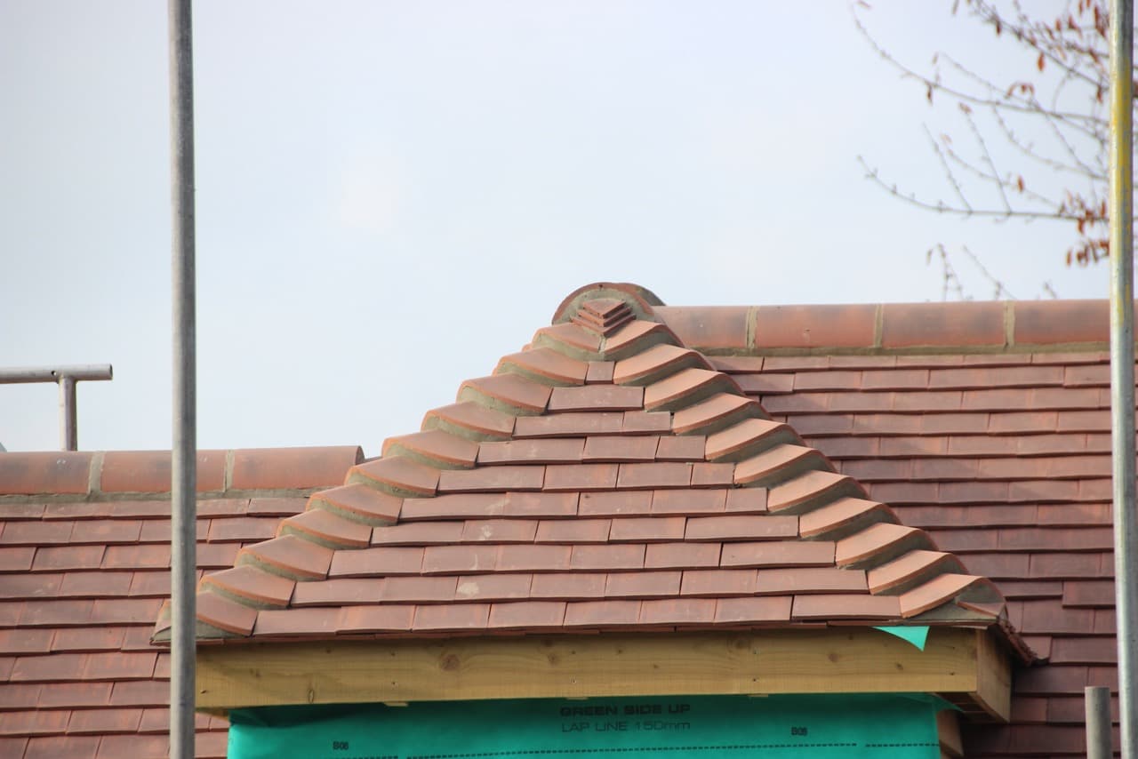 Red clay tiled hip with bonnet hip tiles meeting at the apex, under construction