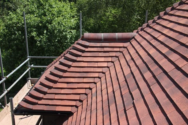 Close-up of a red clay tiled hip roof with bonnet hip tiles and scaffolding